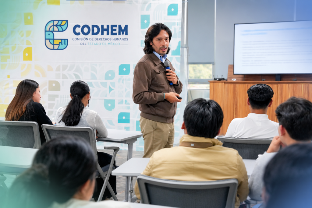 Docente con micrófono imparte una sesión de formación académica ante un grupo de asistentes en un aula de la CODHEM.