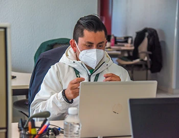 Imagen de una persona sentada frente a una computadora portátil en un entorno de oficina, con objetos de trabajo alrededor. La imagen se utiliza para comunicar que todas las personas indígenas tienen derecho a la identidad cultural, al respeto de su vestimenta, lengua, tradiciones y costumbres, así como a un trato digno, igualitario y no discriminatorio.