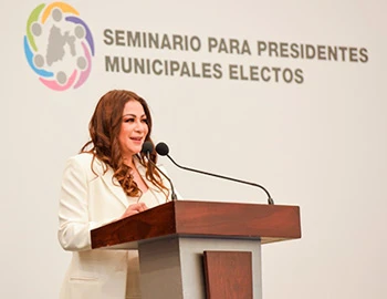 “LLAMA LA PRESIDENTA DE LA CODHEM A LAS Y LOS ALCALDES ELECTOS A EDIFICAR UNA NUEVA ERA PARA LOS DERECHOS HUMANOS. Persona de pie detrás de un podium de madera, hablando frente a un micrófono durante un evento institucional. Al fondo se observa el logotipo y la leyenda ‘Seminario para presidentes municipales electos’