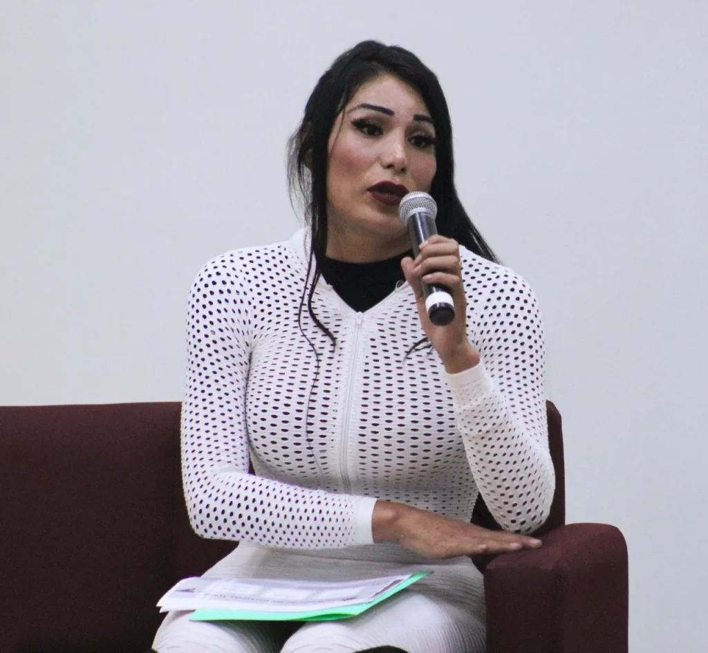 Persona sentada en un sillón, hablando frente al público y sosteniendo un micrófono durante un panel.