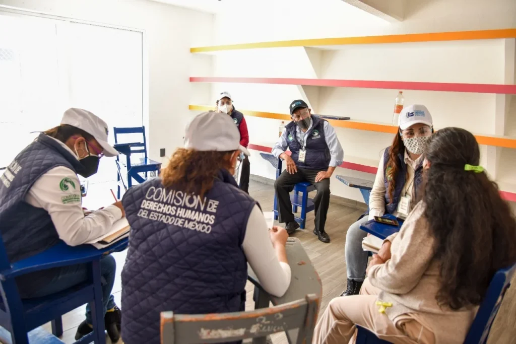 Personal de la Comisión de Derechos Humanos del Estado de México dialoga con personas sentadas en un salón, durante una reunión de atención y escucha.