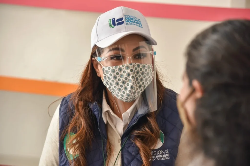 Personal de la Comisión de Derechos Humanos del Estado de México, con equipo de protección, atiende directamente a una persona en espacio interior.
