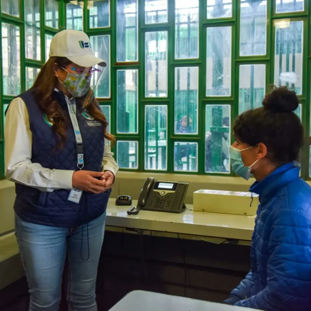 Personal de la Comisión de Derechos Humanos del Estado de México dialoga con una persona sentada en un espacio interior, durante una visita institucional.