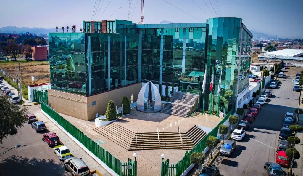 Vista aérea de un edificio institucional moderno con fachada de vidrio y escalinatas de acceso, sede de la CODHEM.