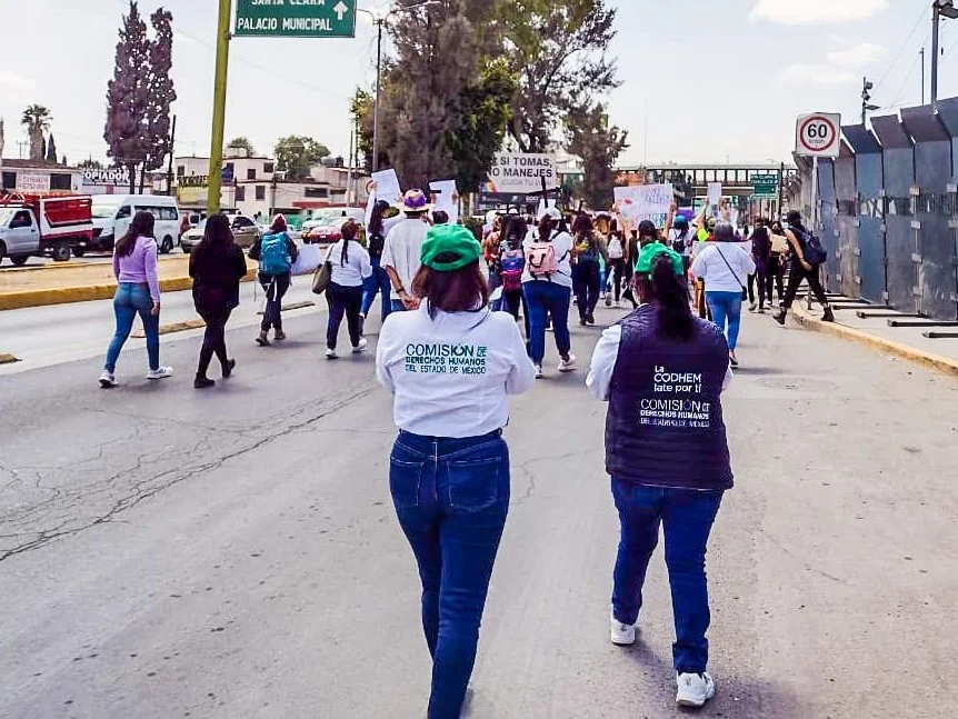 Personas caminan en una marcha por una vía urbana; algunas portan prendas con logotipos institucionales. La CODHEM brindó acompañamiento durante las marchas en el Día Internacional de la Mujer