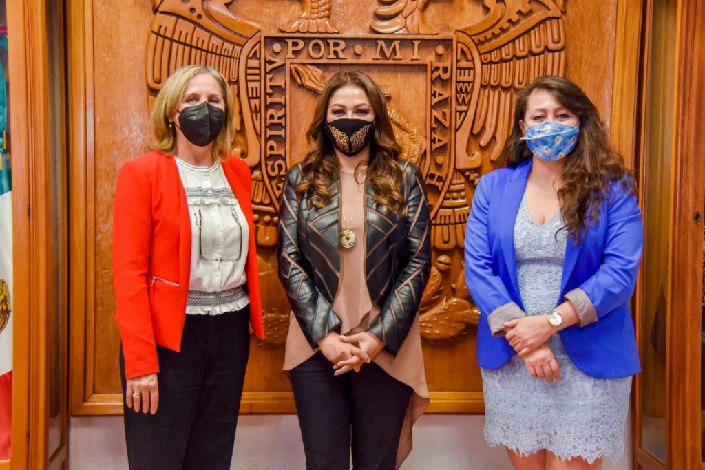 Tres personas posan en una reunión institucional frente a un escudo oficial. La presidenta Myrna Araceli García Morón tuvo una reunión de trabajo con autoridades educativas y destacó el papel de los jóvenes en materia de DDHH