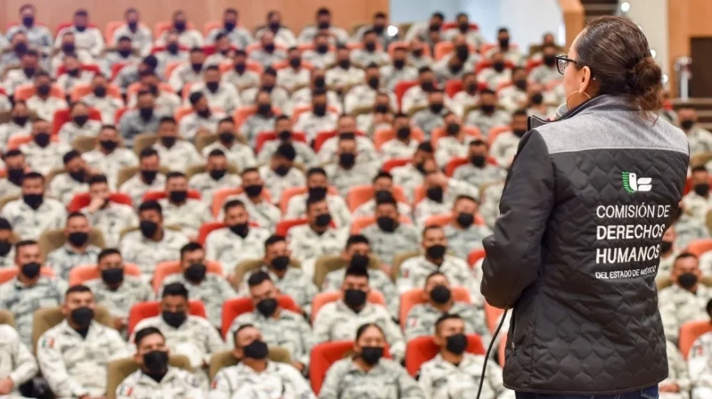 Persona con chaleco institucional se dirige a un auditorio lleno de elementos uniformados. La CODHEM capacitó a 600 elementos de la Guardia Nacional