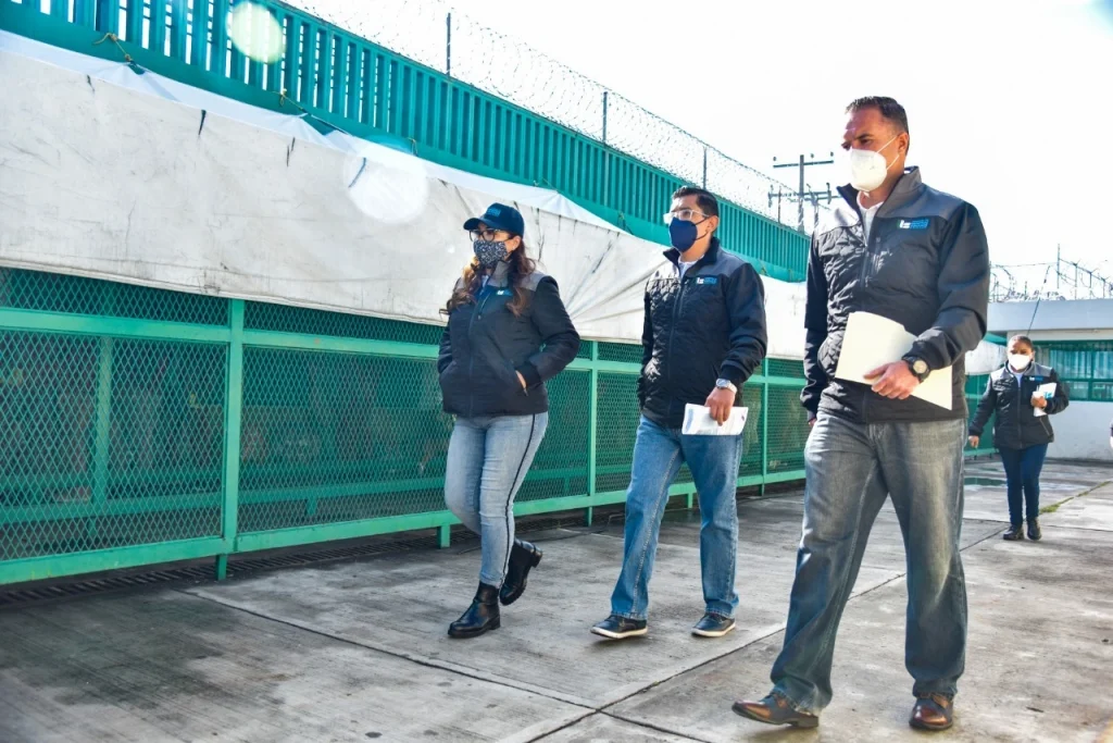 LA PRESIDENTA DE LA CODHEM VISITÓ EL CENTRO PENITENCIARIO DE “SANTIAGUITO”. Imagen de una comitiva caminando por un pasillo exterior dentro de un centro penitenciario, con muros, rejas y alambre de seguridad visibles.