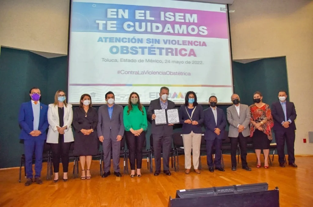 TODOS ESTAMOS COMPROMETIDOS CON LA CERO TOLERANCIA A LA VIOLENCIA OBSTÉTRICA: MAGM. Imagen de un acto institucional con personas en un escenario frente a una pantalla informativa.