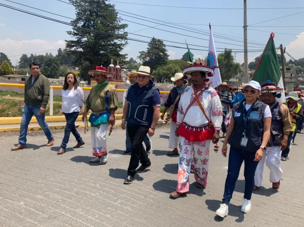 LA CODHEM BRINDÓ ACOMPAÑAMIENTO PERMANENTE A LA CARAVANA DE LA DIGNIDAD Y CONCIENCIA WIXÁRIKA DE JALISCO. Imagen de una caravana caminando por una vialidad, con personas portando vestimenta tradicional y banderas, acompañadas por personal institucional.