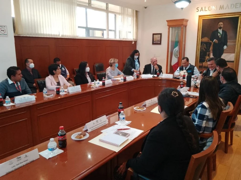 Reunión institucional de defensorías municipales de derechos humanos, con personas sentadas alrededor de una mesa de trabajo en un salón oficial.