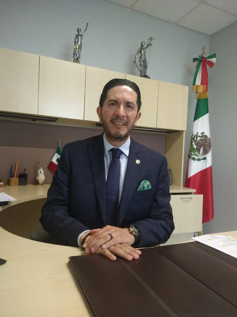 El director de Atención a Grupos en Situación de Vulnerabilidad, Víctor Delgado Pérez, en una oficina institucional, sentada detrás de un escritorio, con bandera de México al fondo. Texto: “LA CODHEM REALIZÓ 235 ACCIONES A FAVOR DE NIÑAS, NIÑOS Y ADOLESCENTES… respeto a la dignidad de la infancia”.