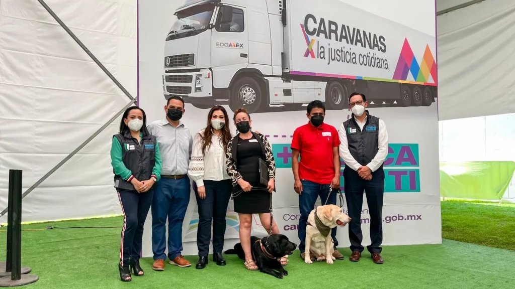 Grupo de personas posando frente a un fondo institucional de las Caravanas por la Justicia Cotidiana, acompañadas por dos perros guía.
