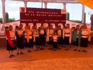 Grupo de personas posa en un acto conmemorativo por el Día Internacional de la Mujer Indígena, frente a un escenario con un cartel alusivo a la fecha.