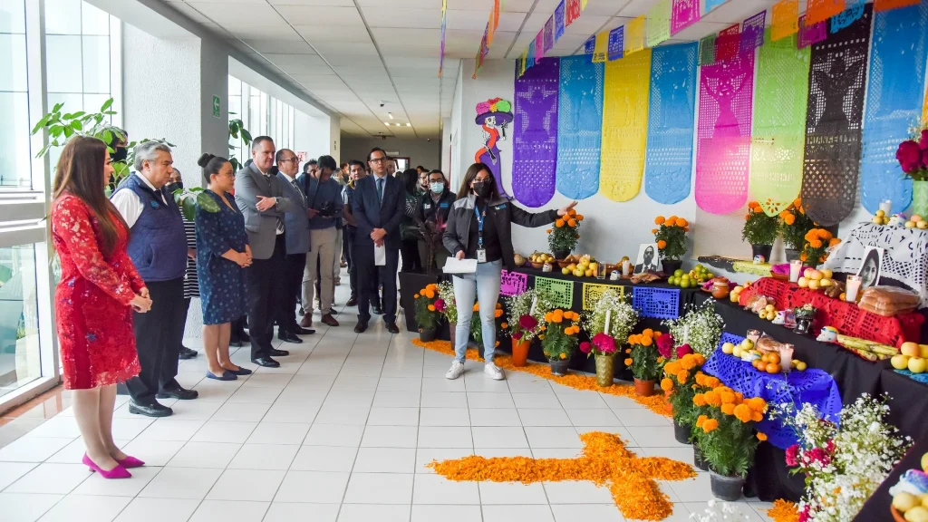 Personas observan una ofrenda tradicional con flores, alimentos y papel picado instalada en un espacio institucional, como parte de una actividad de la CODHEM para promover el derecho humano a la cultura.