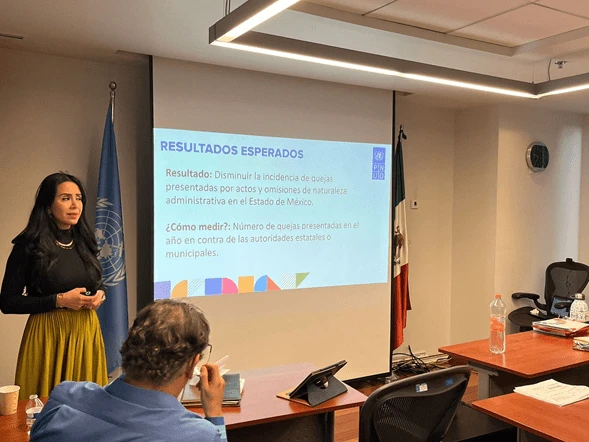 PARTICIPA CODHEM EN INCUBADORA DE EVALUACIONES ORGANIZADA POR PNUD MÉXICO. Exposición en sala de capacitación con una presentación proyectada sobre resultados esperados, personas sentadas escuchando y banderas institucionales al fondo.