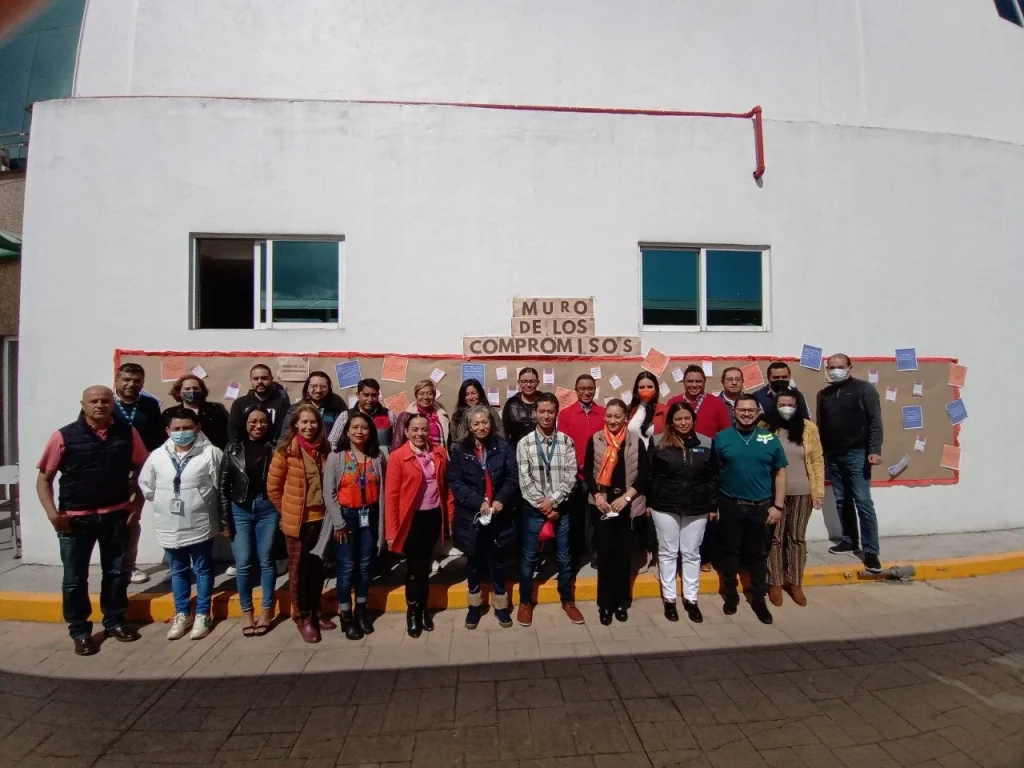 INICIAN 16 DÍAS DE ACTIVISMO EN LA CODHEM CON EL MURO DE LOS COMPROMISOS. Fotografía grupal de personas frente a un muro con mensajes de compromisos en un espacio institucional.