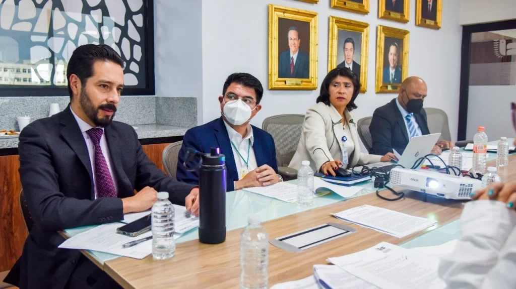 Reunión de trabajo en sala de juntas con personal revisando documentos y equipo de proyección; Juan Laredo Sánchez encabezó el encuentro con personal jurídico y de salud.