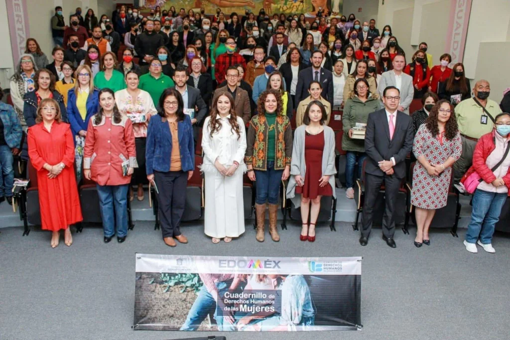 Fotografía grupal en auditorio con decenas de personas posando frente a un banner sobre derechos humanos de las mujeres; el mensaje destaca que el cuadernillo contribuirá a construir sociedades igualitarias y fue presentado por autoridades de la CODHEM y de la Secretaría de las Mujeres.