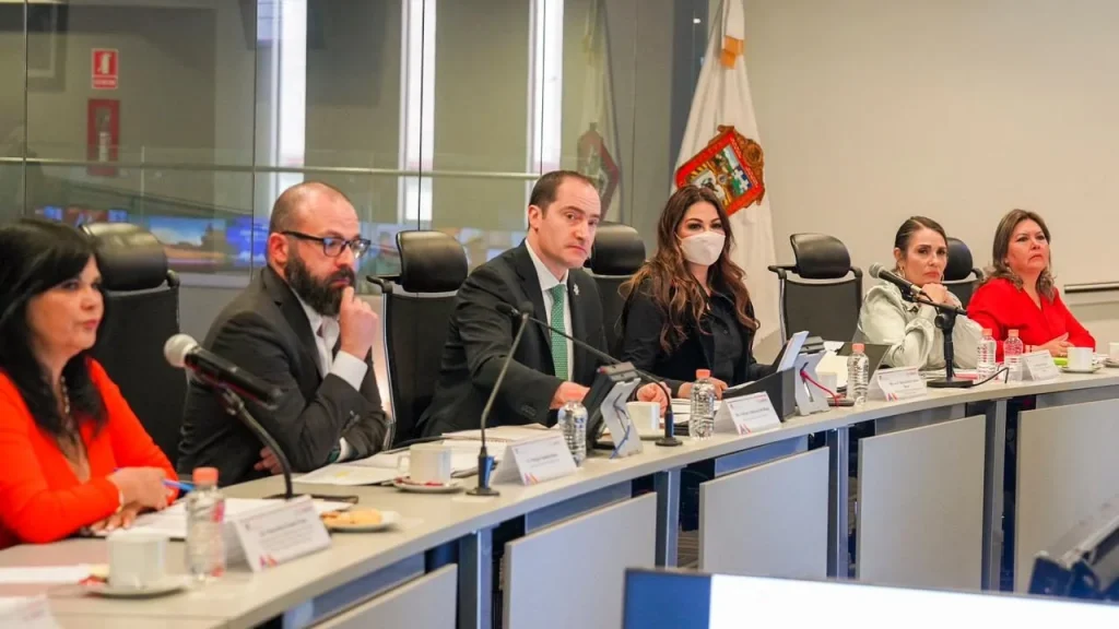 Personas en mesa de reunión institucional con micrófonos y documentos frente a pantallas; CODHEM destaca la importancia de conocer el protocolo de actuación para garantizar derechos de periodistas.