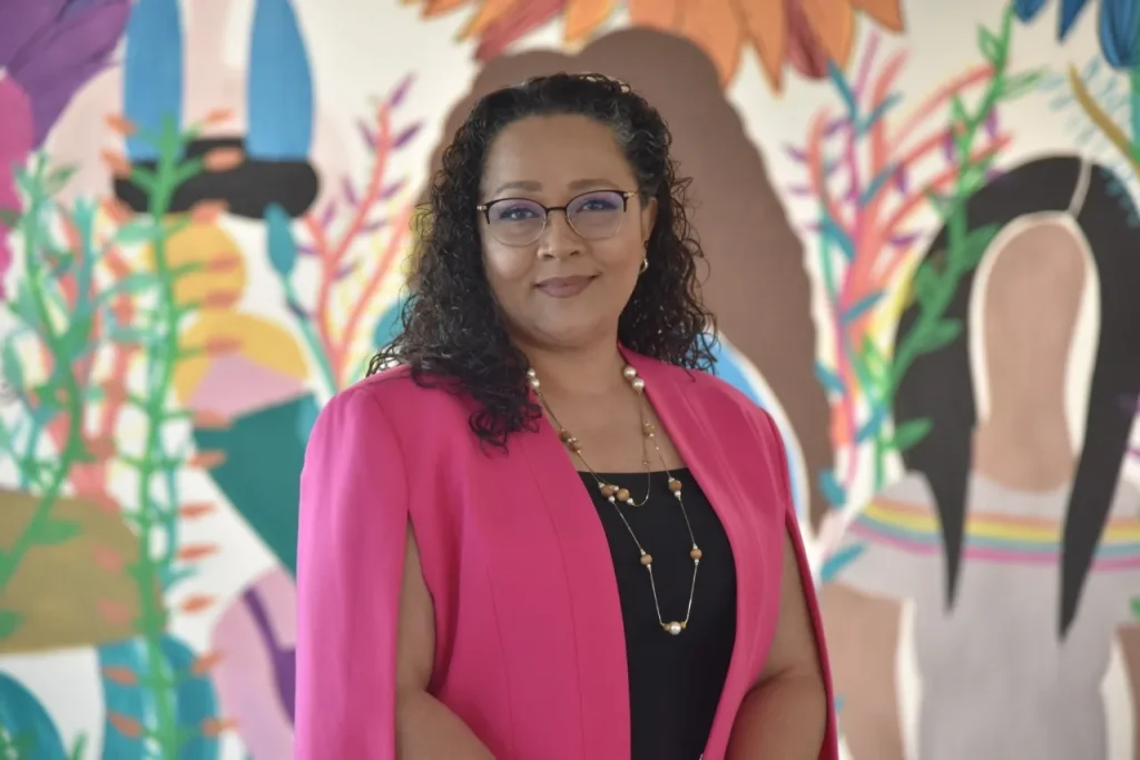 Persona funcionaria posa frente a mural colorido en imagen institucional; la CODHEM sensibiliza a la población sobre el reconocimiento de este derecho humano.