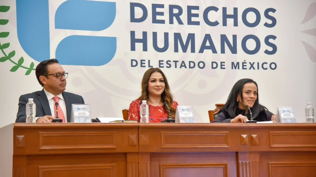 Personas servidoras públicas sentadas en mesa durante sesión institucional; se realiza reunión intermunicipal de defensorías de derechos humanos con participación de la CODHEM y apertura para capacitación.