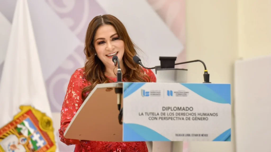 Persona al frente de un podio durante un evento académico con micrófono y logotipos institucionales; inicia diplomado sobre tutela de derechos humanos con perspectiva de género, con participación de personas servidoras públicas.