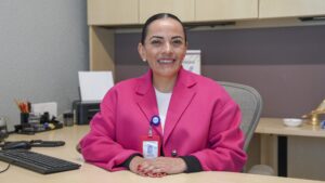 Persona servidora pública sentada en escritorio de oficina con computadora, teclado y mobiliario institucional; espacio de atención donde se brindan servicios y orientación a la ciudadanía.