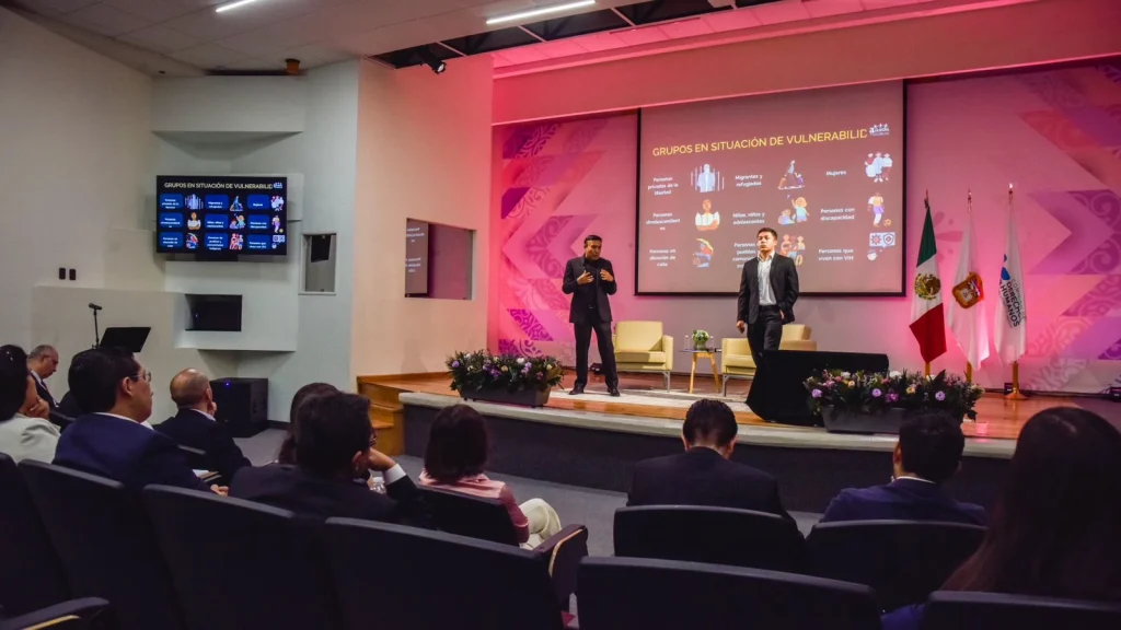Persona facilitadora expone tema sobre interseccionalidad frente a audiencia en auditorio de la CODHEM, con presentación proyectada sobre grupos en situación de vulnerabilidad.