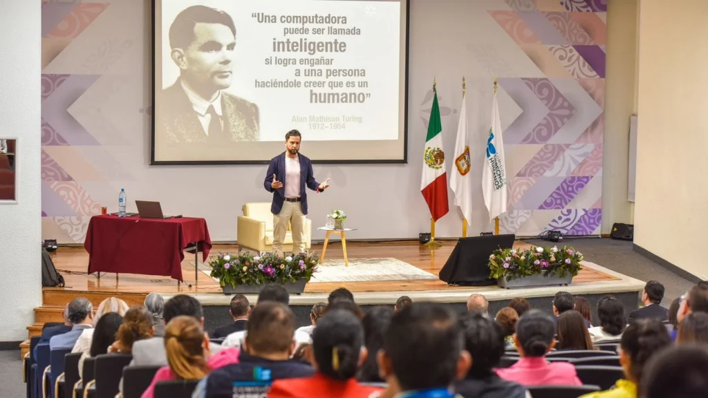 Persona expositora presenta ante un auditorio en un evento de la CODHEM sobre inteligencia artificial, con una diapositiva de Alan Turing y público sentado escuchando la ponencia.