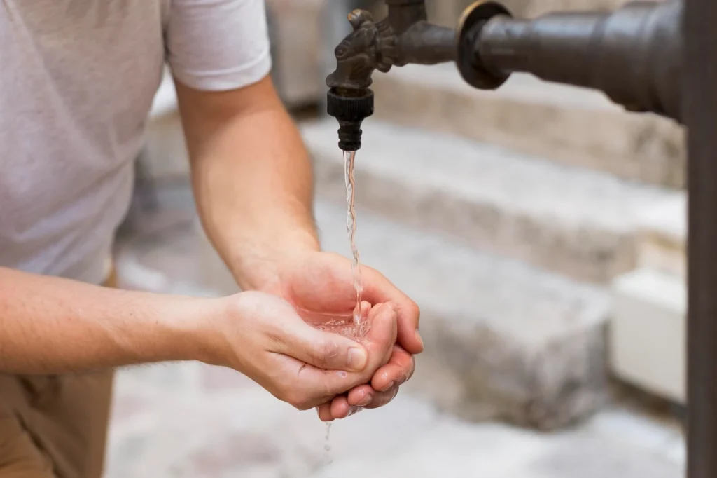 Manos de una persona recibiendo agua de una llave, en alusión al derecho humano al acceso y uso del agua para todas las personas.