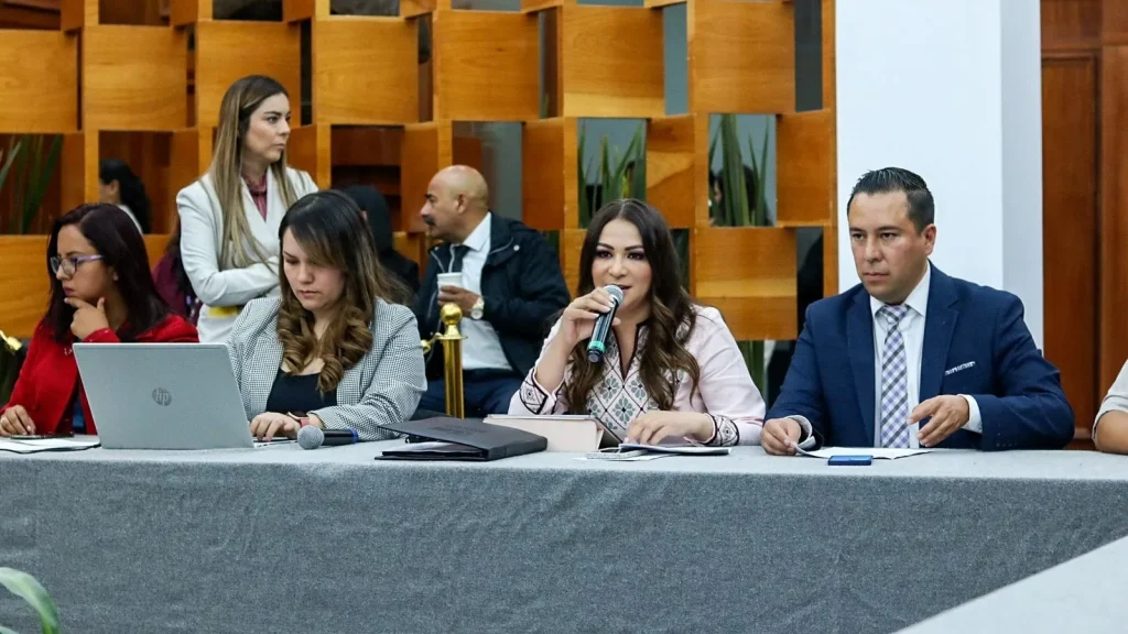 Personas reunidas en mesa de trabajo con equipo de cómputo y micrófono durante una sesión en espacio institucional.