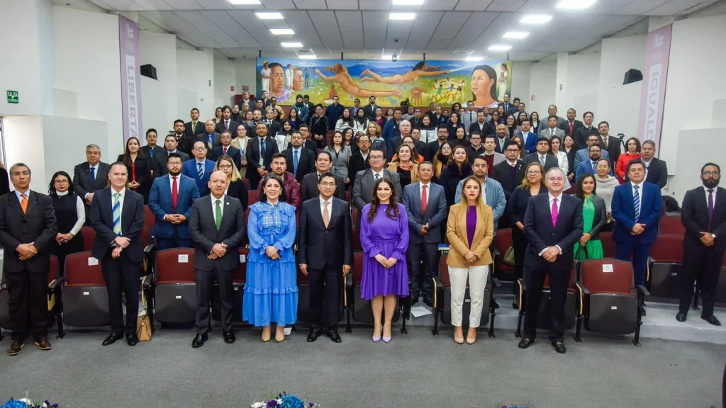 Fotografía grupal en un auditorio con filas de asientos escalonados donde numerosas personas están de pie organizadas en varias filas para una toma formal