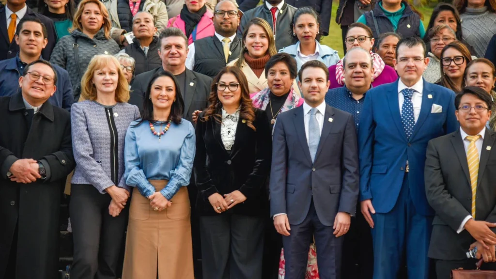 Grupo numeroso de personas posando en filas para una fotografía oficial al aire libre, con vestimenta formal como trajes, blazers y vestidos, frente a un entorno institucional.