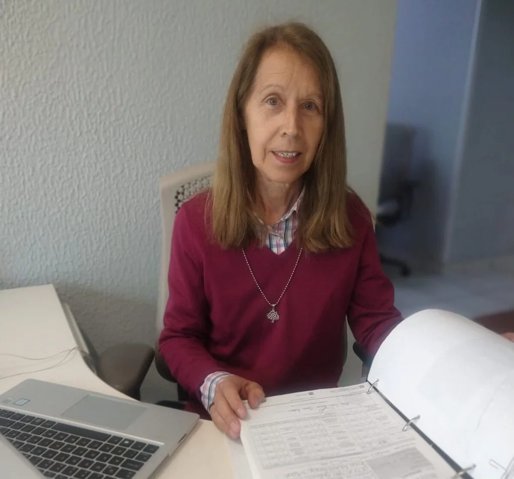 Persona sentada en un escritorio con una computadora portátil abierta y un archivador de hojas, mostrando documentos mientras se encuentra en una oficina.