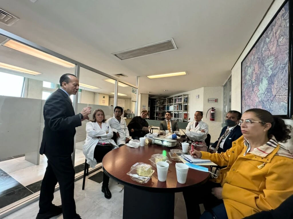 Grupo de profesionales en un espacio de oficina reunidos alrededor de una mesa redonda, con proyector y documentos, durante una presentación técnica.