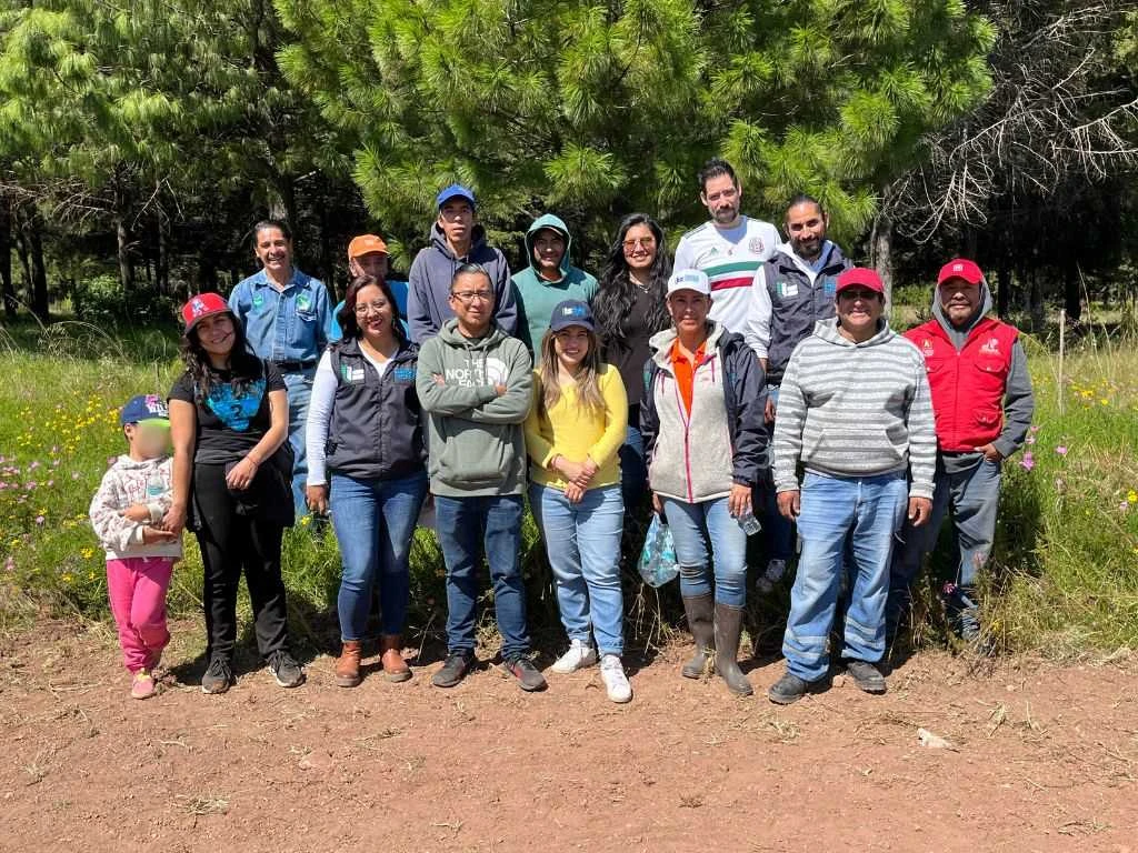 Grupo de personas posando en un área natural frente a árboles de pino; varias llevan gorras y ropa de campo, reunidas después de una actividad al aire libre en un entorno boscoso.