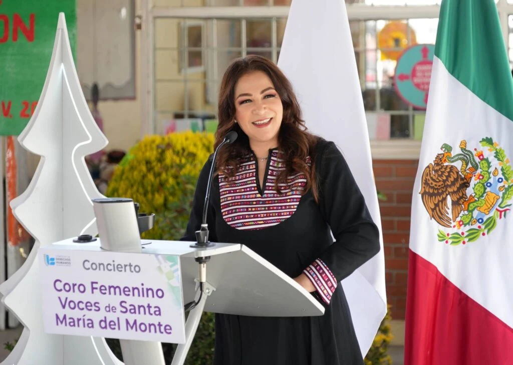 Presentación artística en un escenario escolar donde un grupo de estudiantes canta frente a una audiencia sentada, bajo una estructura con decoraciones coloridas y figuras colgantes.
