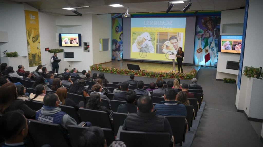 Personas sentadas en butacas dentro de un auditorio durante un evento. En primer plano, varias personas observan hacia el frente, vestidas con ropa formal. En el fondo se aprecian más asistentes distribuidos en filas, con iluminación uniforme y mobiliario tipo sala de conferencias.