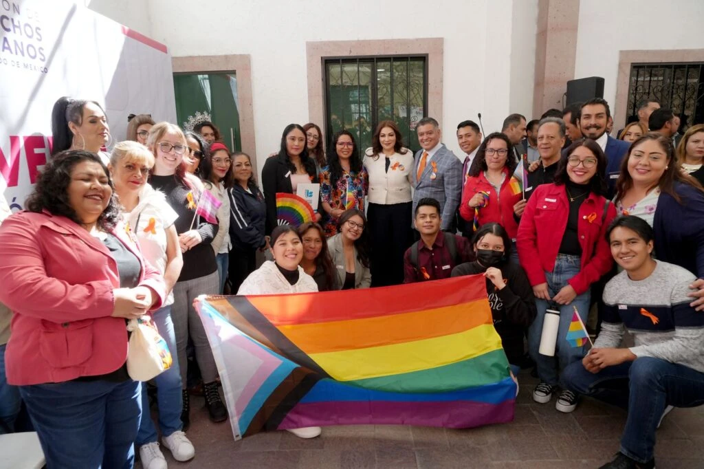 Dos personas de pie muestran documentos enmarcados durante un evento institucional. Detrás se observa un panel con el texto “COA Calco Gobierno Municipal 2025–2027” y “Firma de convenio”. A un lado, otra persona aplaude. La escena está iluminada con luz natural en un espacio exterior o semiabierto.