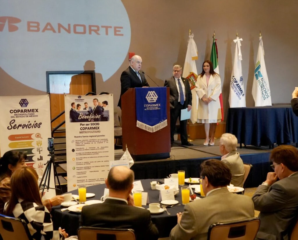 Escenario de conferencia con una persona hablando en un podio frente a asistentes sentados, acompañado de otra persona a un lado y con logotipos de COPARMEX y BANORTE visibles.