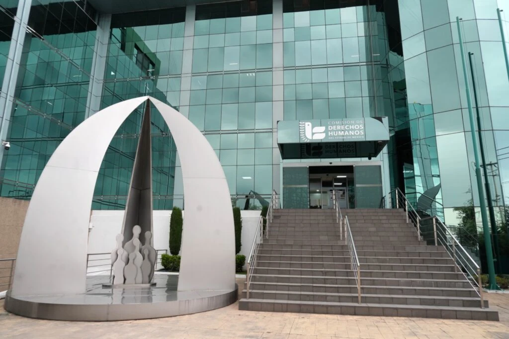 Vista exterior del edificio sede de la Comisión de Derechos Humanos del Estado de México. La construcción presenta una fachada de cristal verde reflectante y una escalinata de acceso con barandales metálicos.