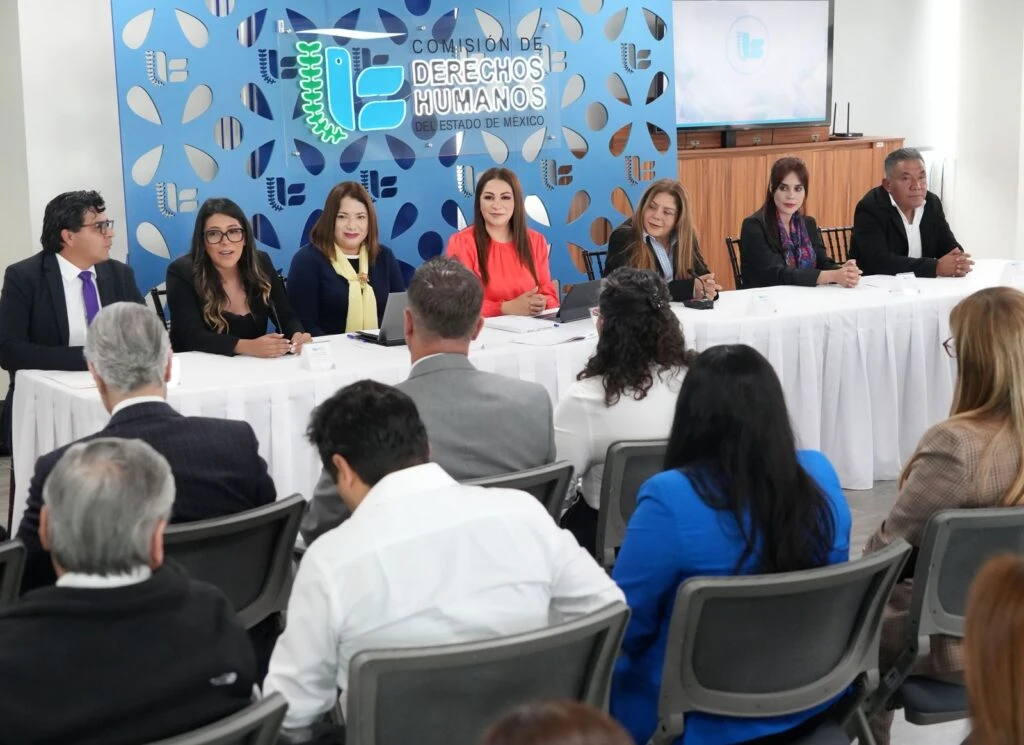 Sesión institucional de la Comisión de Derechos Humanos del Estado de México con personas ponentes al frente de una audiencia en una sala de reuniones.