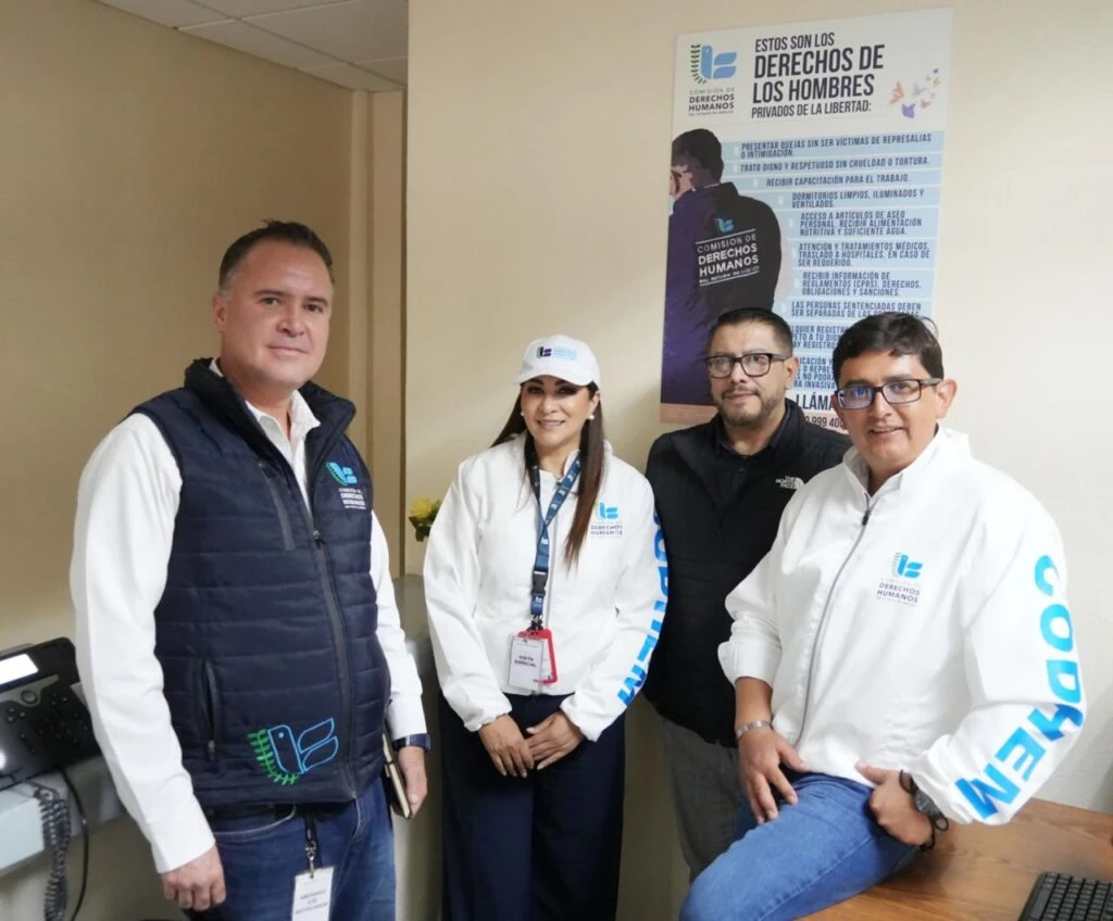 Cuatro personas posan en el interior de una oficina junto a un cartel informativo sobre los derechos de las personas privadas de la libertad. Varias de las personas portan prendas institucionales de la Comisión de Derechos Humanos del Estado de México.
