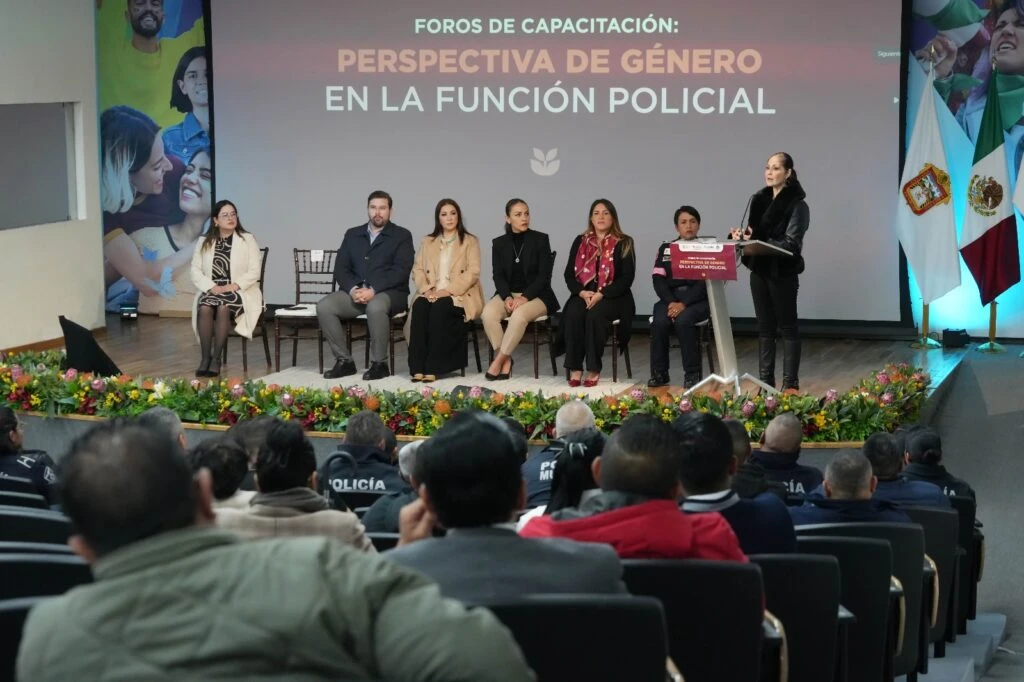 Foro de capacitación sobre perspectiva de género en la función policial celebrado en un auditorio. En el escenario, varias personas participan en un panel mientras una persona interviene desde un atril. Detrás se proyecta el título “Foros de Capacitación: Perspectiva de Género en la Función Policial”. En primer plano se observa al público asistente, integrado principalmente por personal de corporaciones policiales.