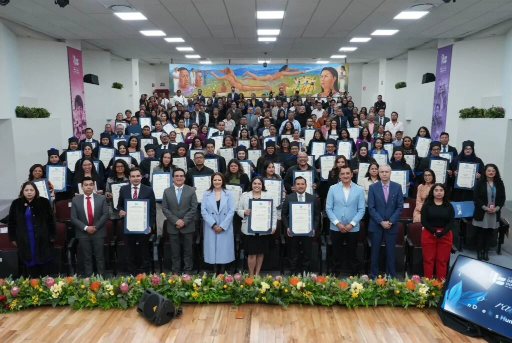 Persona pronunciando un discurso desde un atril en el escenario de la Comisión de Derechos Humanos del Estado de México. Al fondo se observa una mesa del presídium con varias personas sentadas, así como la identidad gráfica institucional y decoración floral en la parte frontal del escenario.