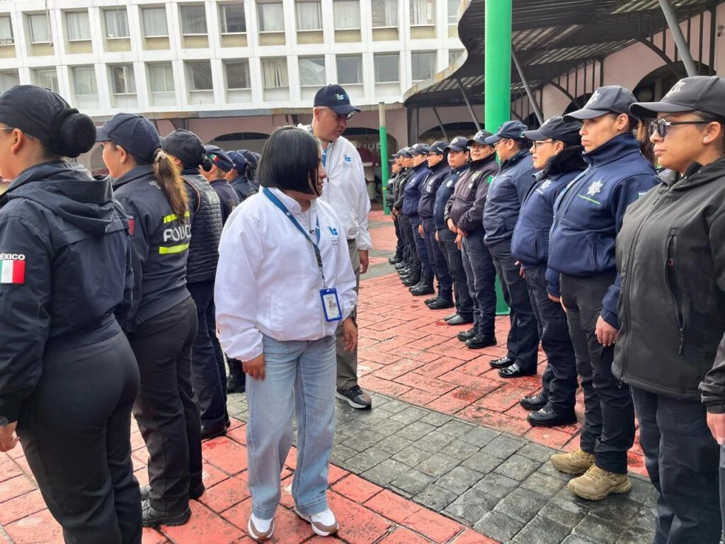 Recorrido de supervisión en una plaza urbana con presencia de personal de seguridad y protección. Varias personas portan chamarras institucionales y uniformes mientras se desplazan entre los contingentes formados.