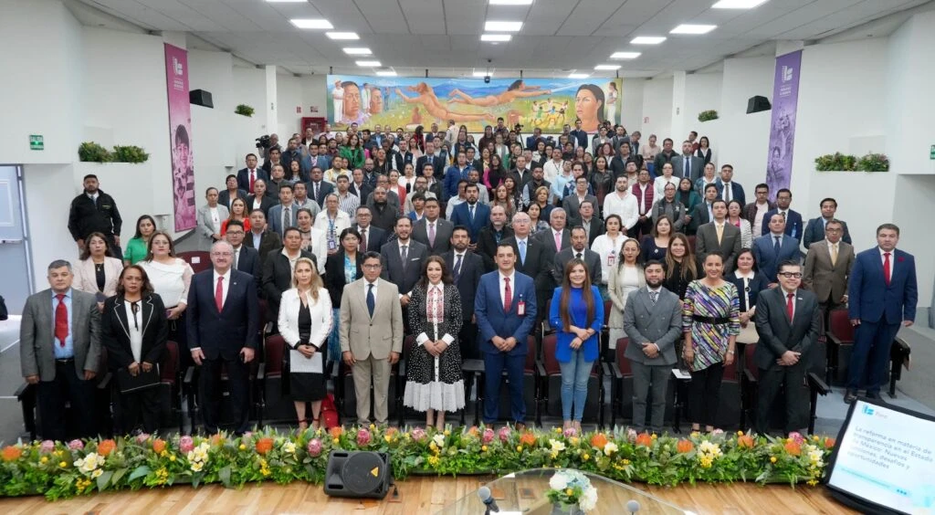 Fotografía grupal de participantes de un foro académico realizado en el auditorio de la Comisión de Derechos Humanos del Estado de México. Las personas se encuentran distribuidas en distintos niveles del recinto frente al escenario principal decorado con arreglos florales.