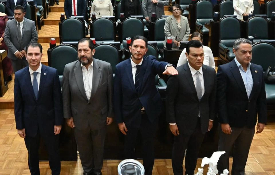 Inicia CODHEM nueva etapa con nombramiento de Víctor Leopoldo Delgado Pérez como presidente para el periodo 2025-2029. Vista elevada de una ceremonia institucional en un salón con butacas, donde cinco personas vestidas con traje se encuentran al frente del recinto mientras otras personas observan desde las filas posteriores.