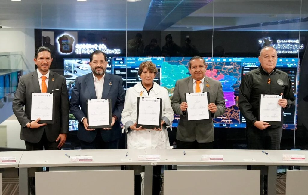 Personal de la Comisión de Derechos Humanos del Estado de México mantiene diálogo con elementos de seguridad y una persona ciudadana en un espacio público. Al fondo se aprecian áreas verdes y un edificio histórico con campanario.
